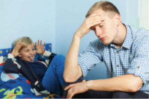 man holding his head with child misbehaving in background